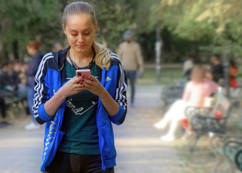 18 - Young woman with a blue athletic zip-up track jacket featuring white three-stripe accents along the sleeves